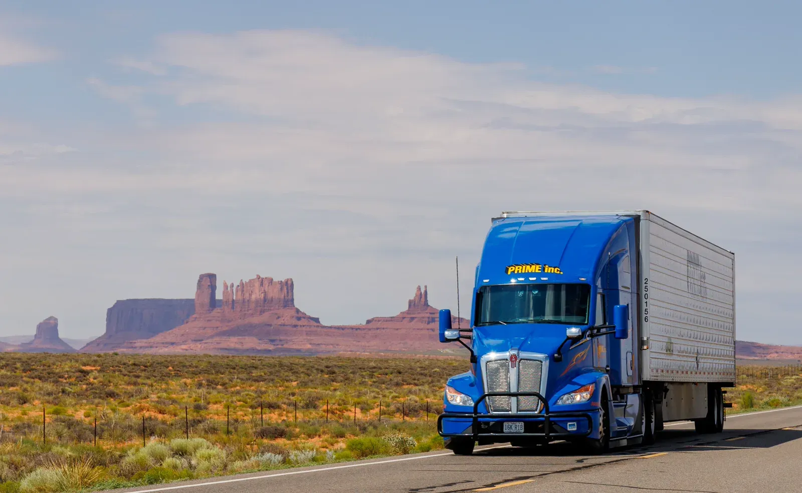 Blue Prime Inc. semi truck driving on a desert highway past red rock buttes